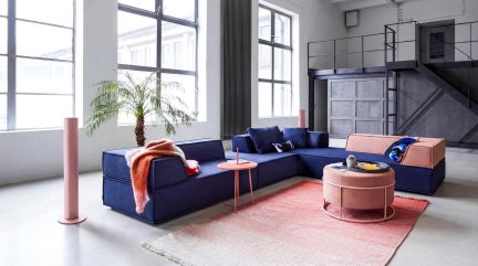 Modulaire blauwe en roze hoekbank in een loftwoonkamer, met ronde roze salontafel op een roze-wit kleurverlooptapijt
