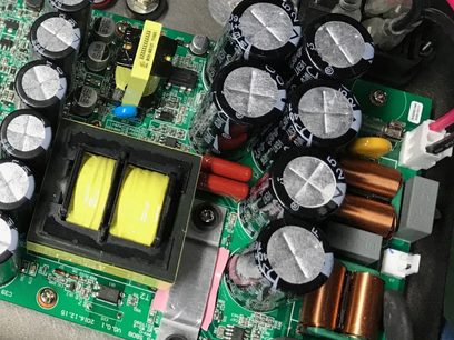 Zelený plošný spoj s různými elektronickými součástkami: stříbrné kondenzátory, barevné rezistory, černé čipy