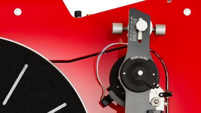 Plato giradiscos hi-fi Vertere Acoustics Pack DGX Sabre rojo con chasis de metal lacado, vista en primer plano desde arriba mostrando el borde del plato negro y la base del brazo de lectura en negro y plateado con escala de ajuste y cables multicolores