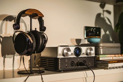 Hi-fi, circumaurale hovedtelefoner på stativ ved siden af en sølvfarvet hovedtelefonforstærker på en hyldeenhed i stuen