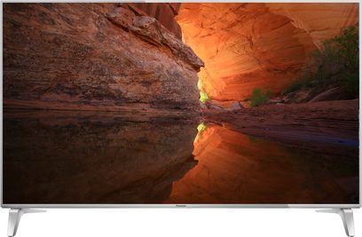 Panasonic TX-65DX750E-tv, der viser et billede af en orange klippekløft med refleksioner på skærmen, set forfra på sølvfarvet fod