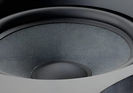 Detailní šikmý záběr reproduktoru s texturovanou membránou v antracitově šedé barvě, centrálním dómem a černým pružným závěsem