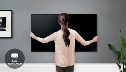 Billedet viser en kvinde set bagfra foran en Samsung-tv, der er monteret på væggen med en WMN-M13EA/XC vægbeslag, i et moderne interiør