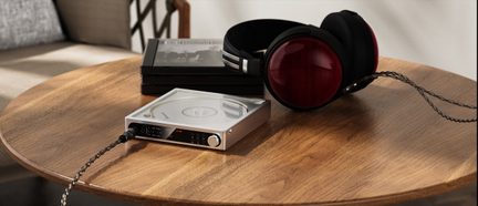 Hi-Fi-Kopfhörer in Schwarz mit roten Ohrmuscheln und silbernem Verstärker auf rundem Holztisch