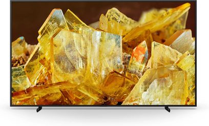 Sony XR98X90L TV, fladskærm, set forfra, gennemsigtige gule krystaller, sort ramme, sorte fødder, brun baggrund