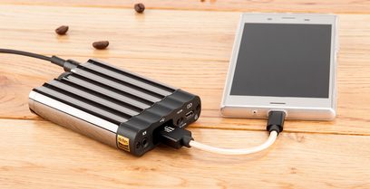 Bærbar iFi Audio xDSD sort lydkonverter, kabelforbundet til en hvid smartphone, der ligger på et træbord