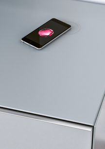 Czarny smartfon z wyłączonym ekranem leżący na jasno szarym meblu audio-wideo Spectral Scala SC1657, częściowy widok z góry