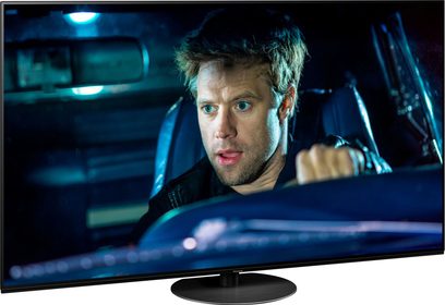 Téléviseur Panasonic TX-55HZ1000E allumé affichant en gros plan le visage d'un homme aux yeux bleus et cheveux blonds ébouriffés