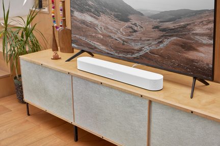 Hvid Sonos-soundbar placeret under et tv på et moderne tv-møbel i lyst træ