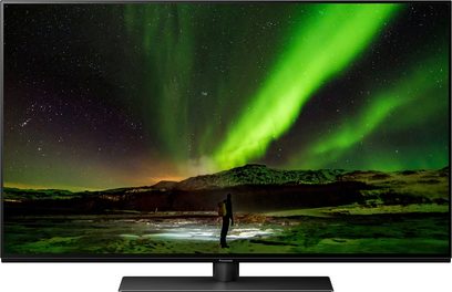 Panasonic TX-48JZ1500E-tv, der viser et grønt nordlys over bjerge, med en person stående foran en frossen sø