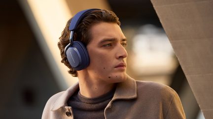 Mattschwarzer Over-Ear-Kopfhörer aus Kunststoff in Blau, gepolsterter Textil-Kopfbügel und Metallscharnier, gewölbte Ohrmuschel in der linken Seitenansicht sichtbar