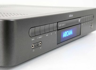 Metalinės pilkos spalvos Arcam Solo Movie 5.1 Blu-ray grotuvas, priekinėje dalyje mėlynas "ARCAM" ekranas, mygtukai ir diskų skyrelis