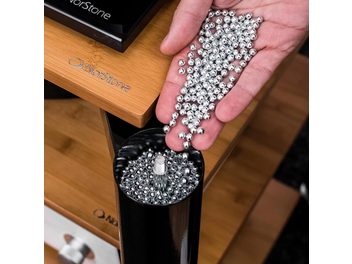 Bolas metálicas Norstone Acoustic Metal Beads, mano sosteniendo un accesorio acústico esférico compuesto por numerosas pequeñas bolas plateadas brillantes