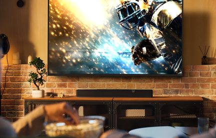 Černý televizní soundbar pod velkou obrazovkou v cihlovém obývacím pokoji, moderní domácí kino instalace
