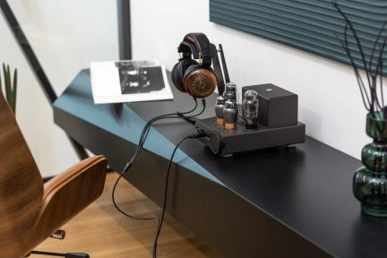 Černý lampový sluchátkový zesilovač se sluchátky s dřevěnými mušlemi položený na černém nábytku