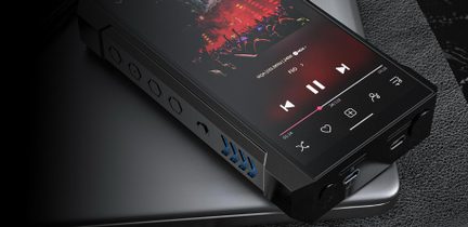 Rektangulær svart digital musikkspiller i metall, sett i skrått perspektiv, berøringsskjerm påslått med lydgrensesnitt, sidekant med fem sekskantede knapper og et blått ventilasjonsgitter i chevron-mønster