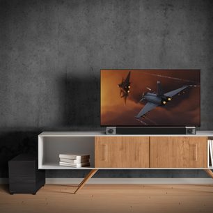 Klipsch Cinema 400 sort soundbar i sort under et lyst træmøbel til TV, med en fladskærm der viser et gråt militærfly i luften