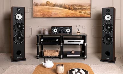 To svarte høyttalere, et svart audioskap med platespiller, forsterker og CD-spiller, et landskapsbilde på veggen, et beige teppe på gulvet