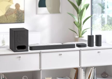 Set di altoparlanti neri composto da una soundbar, un subwoofer e 3 diffusori satelliti su mobile bianco