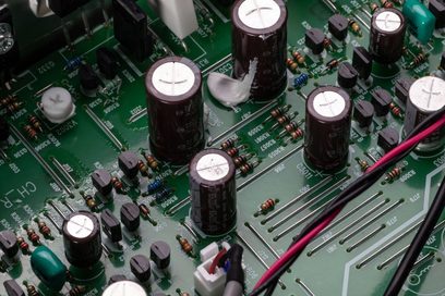 Zaļa drukātā shēma ar vairākiem melniem elektrolītiskiem kondensatoriem un brūnām pretestībām, tuva augšējā skata perspektīva