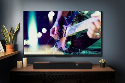 Fernseher, der Hände zeigt, die E-Gitarre spielen, auf einem Holzmöbel mit zylindrischen Kerzen davor stehend