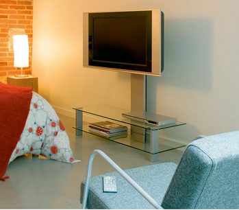 Tv-møbel i glas og metal med hylder, drejelig tv-holder, i en stue med sofa, puder, mur af mursten og lampe