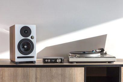Hvid højttalerkabinet, sølvfarvet pladespiller og Octavio AMP 32V hi-fi stereoreceiver i træ på lys træhylde