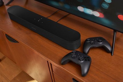 Soundbar nera Sonos su mobile TV in legno con due controller di gioco neri davanti a uno schermo piatto