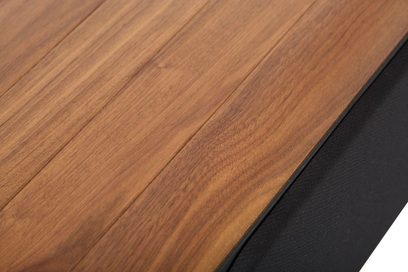Primo piano dell’altoparlante, cabinet in noce marrone satinato con doghe unite, lato rivestito da una griglia in tessuto nero, vista dall’alto inclinata