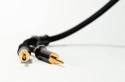 Cavo audio Advance Paris nero con guaina flessibile, vista ravvicinata obliqua su un connettore RCA maschio e un connettore RCA femmina in metallo nero con terminali placcati oro e scritte dorate