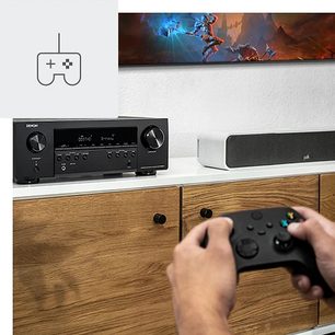 Denon AVC-S660H sort hjemmebiografsforstærker, set forfra og ovenfra, med en trådløs gamekontrol oven på, med tændt skærm der viser et videospil