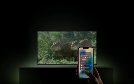 Televisore a schermo piatto con dinosauri sullo schermo e iPhone in primo piano che controlla la riproduzione tramite Apple TV