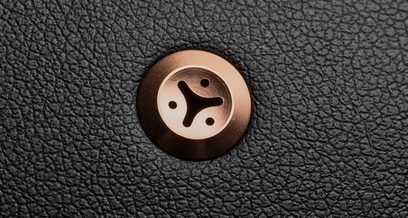Rund træknap med yin-yang-mønster indgraveret i midten, placeret på en ru, sort kornstrukturet overflade