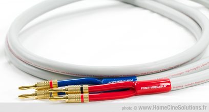 Højttaler-kabel fra Positive Cable Norma, rødt og blåt, med forgyldte bananstik, liggende på et oprullet hvidt kabel