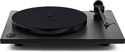 Juoda Rega RP78 vinilinių plokštelių grotuvė, apvalus padėklas, tonarinė galvutė ant svarstiklio, stovi ant juodo stačiakampio pagrindo, matoma iš viršaus ant balto fono