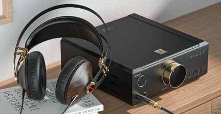 Tamsaus medžio, juodos dirbtinės odos ir auksinio metalo aplinkausiai ausinės, padėtos ant knygų ir prijungtos laidu prie matinio juodo metalo stalininio stiprintuvo su didele auksine garsumo rankenėle, apjuosta mėlynu šviesos žiedu, vaizdas iš trijų ketvirčių perspektyvos