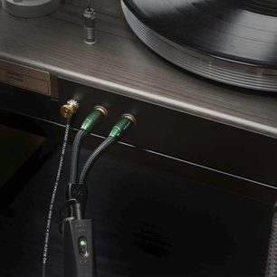 Phono-kabel Black Hole GroundGoody 1,5m med grønne metalstik forbundet til en pladespiller på en træoverflade