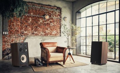 Interiér ve stylu loftu s cihlovou zdí, okny s mřížemi, vintage koženým křeslem a stolem, dřevěnými hi-fi reproduktory