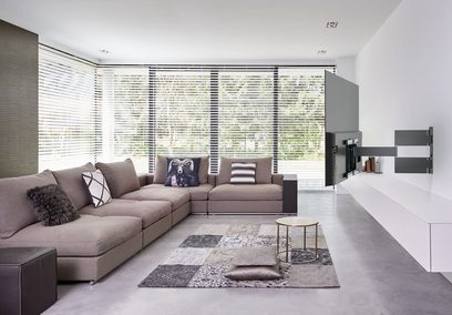 Moderne stue med grå hjørnesofa, dekorative puder, tæppe, rund sofabord og horisontale venetianske persienner