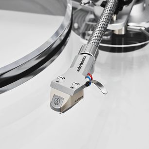 Nærbillede, let set oppefra, af det beige pickuphoved og den flettede sølvfarvede metalarm på Audio Technica AT-LPA2 hi-fi pladespiller, headshell med logo, farvede kabler og synlig nål
