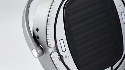 Side close-up of the Audeze LCD-S20 closed-back wired hi-fi headphones, featuring a satin-finished silver-gray metal frame with a perforated articulated yoke and a black oval earcup fitted with a fine grille