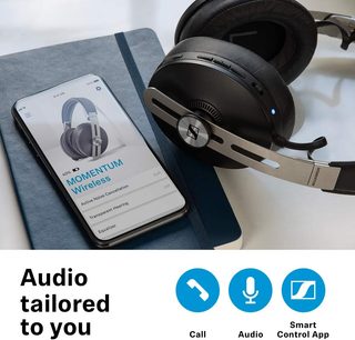 Bezdrátové sluchátka Sennheiser Momentum 3 Wireless s obepínací konstrukcí v černé barvě položená na brožuře s technickými specifikacemi a smartphone zobrazující ovládací aplikaci
