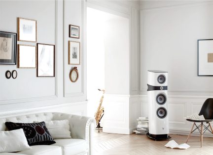 Helles Wohnzimmer mit weißem Sofa, Kissen, Rahmen, Saxophon, weißem Lautsprecher, schwarzem Stuhl, hellem Parkett, verzierten Wänden