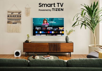 Smart TV Tizen på træmøbel, grøn sofa, grøn plante, makramé-vægdekoration, hvid højttaler