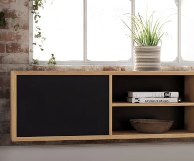 Wandmöbel aus hellem Holz mit schwarzer Front und offenen Regalen, frontal gesehen, dekoriert mit einer Pflanze im geflochtenen Topf, Büchern und einer Schale