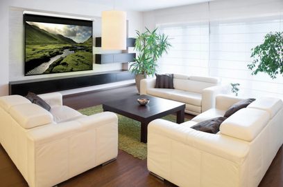 Moderne stue med beige sofaer, mørkt træbord, grønne planter og en stor fladskærm på væggen, der viser et bjerglandskab med en flod