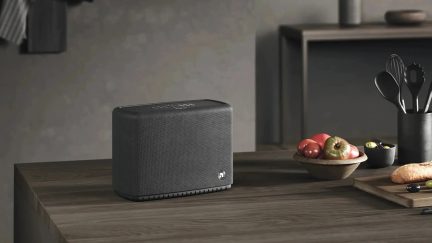 Altavoz negro rectangular con rejilla frontal y controles en la parte superior, colocado sobre una encimera