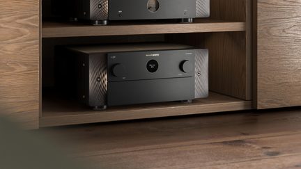 Melns Marantz mājas kinozāles pastiprinātājs ar teksturētu alumīnija priekšpusi, iebūvēts gaiša koka TV skapī