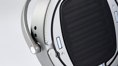 Seitliche Nahaufnahme des geschlossenen, kabelgebundenen HiFi-Kopfhörers Audeze LCD-S20 mit silbergrauem Metallgehäuse in satinierter Ausführung, schwenkbarer gelochter Gabel und schwarzer ovaler Ohrmuschel mit feinem Gitter.