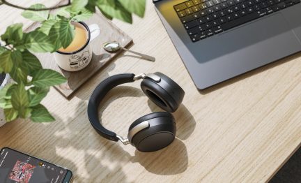 Μαύρα ακουστικά over-ear, πλαστικό και μέταλλο, με επενδεδυμένο σκελετό κεφαλής, ματ φινιρίσματα, θέα από πάνω σε ξύλινο γραφείο